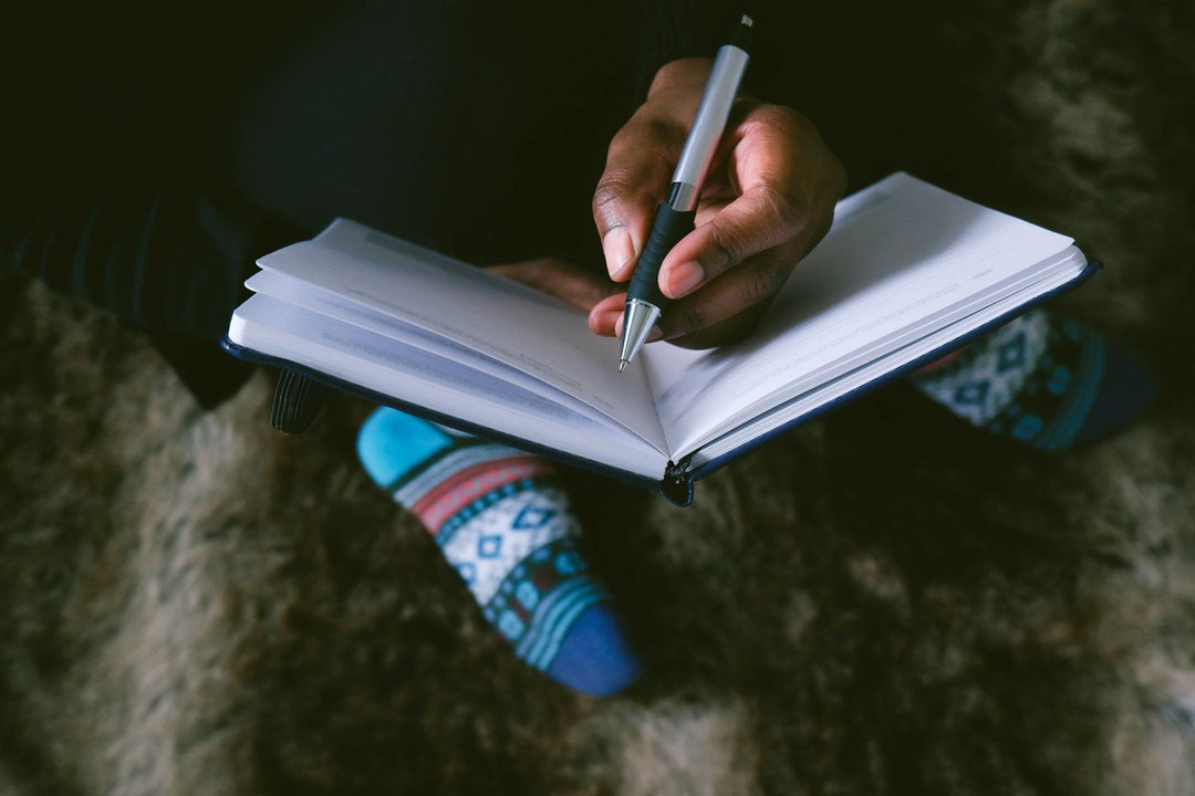 person writing in a journal with crossed legs